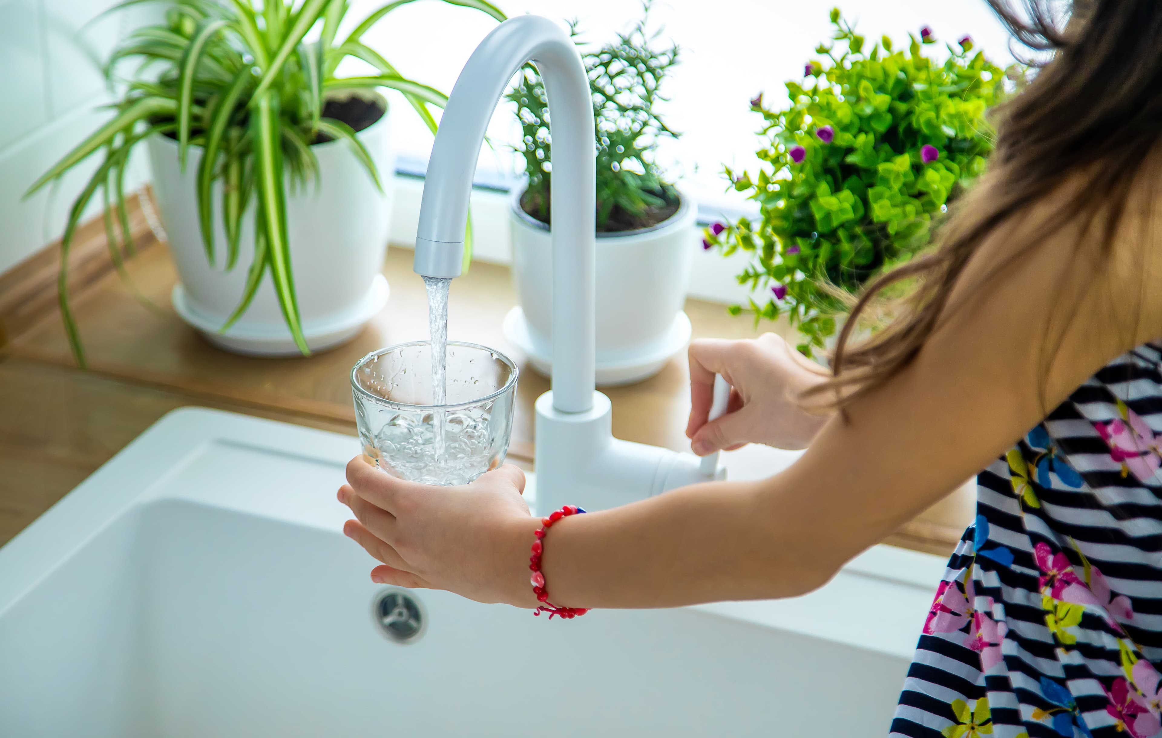 Child filling a glass of clean water from kitchen faucet